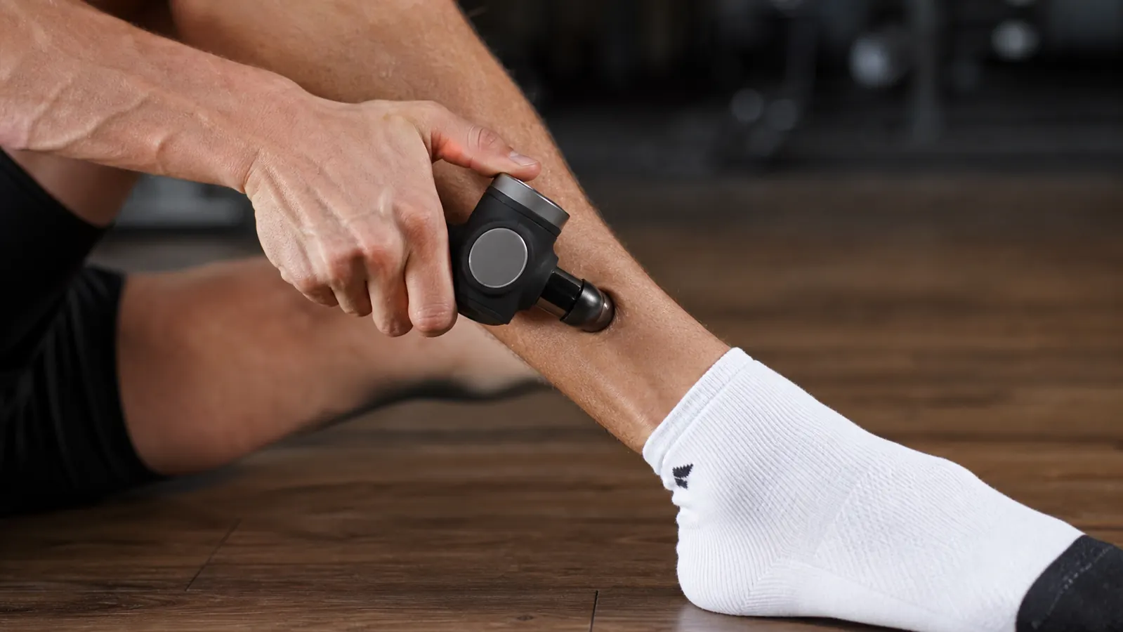 Person sitting on a couch at home using the Theragun Relief on their calf after an evening run, in comfortable clothes